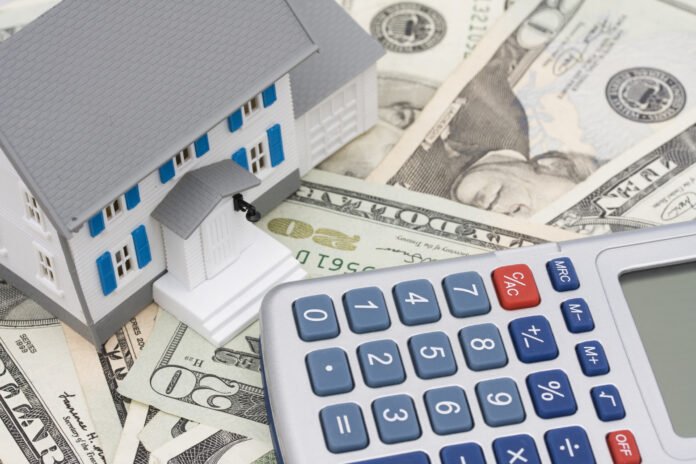 Being a Successful Private or Hard Money Lender Lots of 20 dollar bills with a model of a house with a grey roof and blue shutters and a calculator